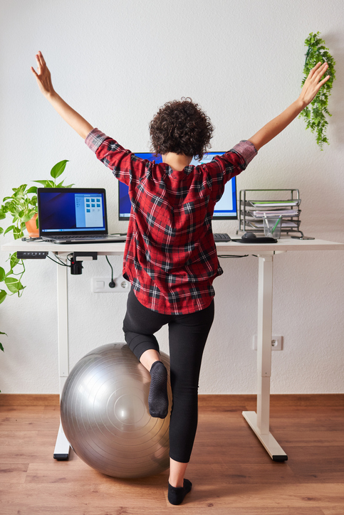 Person incorporating a balance and mobility exercise beside a standing desk to reduce stiffness and encourage position changes during the workday.